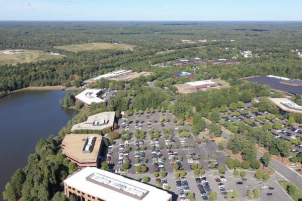 Aerial view: office park, buildings, parking lots, lake, trees.